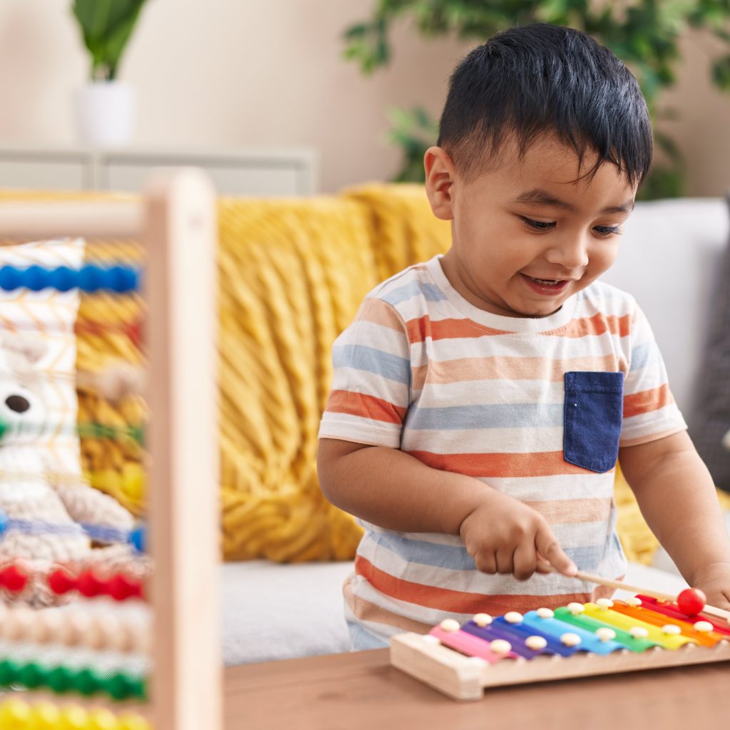 Adorable hispanic toddler playing xylophone standing at home