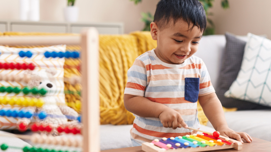 Adorable hispanic toddler playing xylophone standing at home